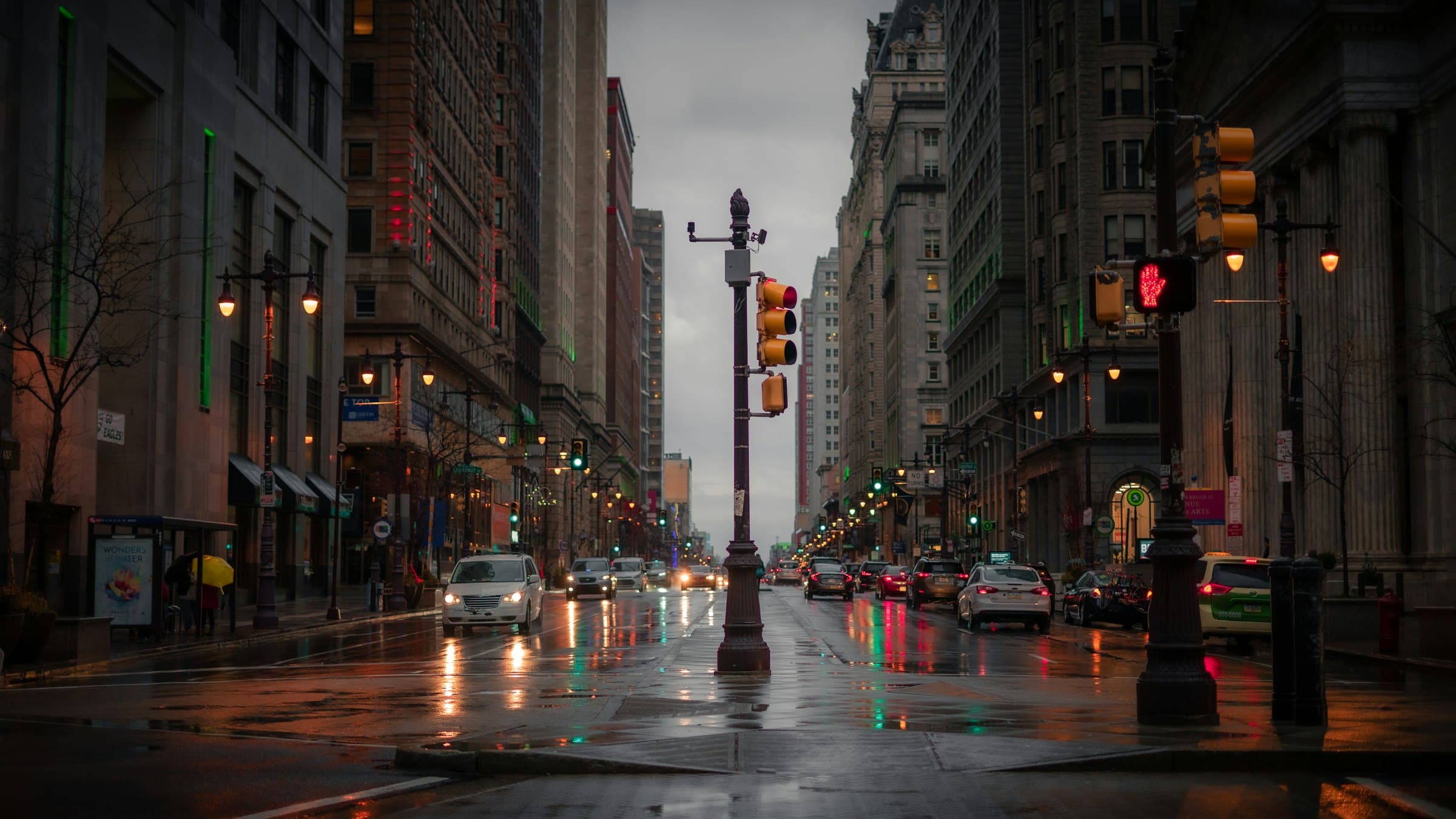 A city avenue at dusk after rain, lights coming on